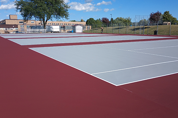 Revitalized tennis courts at Waterloo West High School featuring smooth, brightly colored surfaces after crack repairs, bird bath restoration, and acrylic resurfacing, with one court also striped for pickleball.