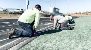 In-house crew installing a synthetic running track surface over a prepared base.