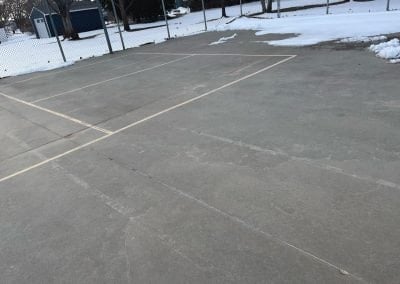 Damaged tennis court with faded lines and patches under snow