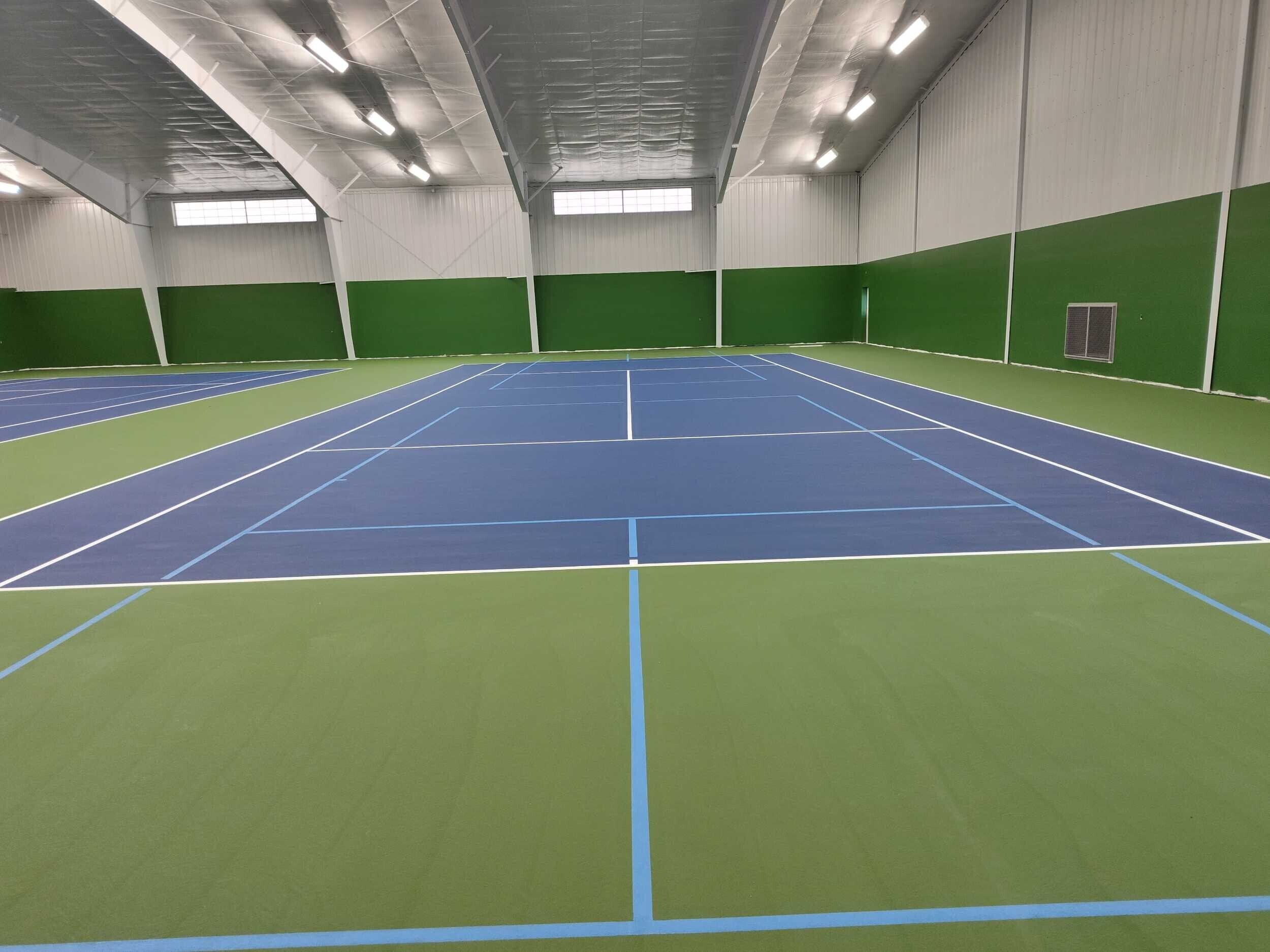 Indoor tennis court with bright lighting and smooth acrylic surface