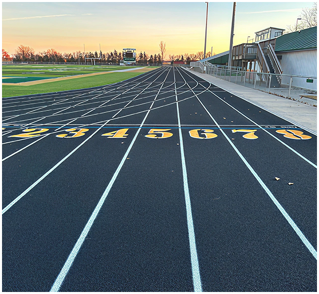 Professional running track resurfacing and repair with precision latex surface finish by Pro Track & Tennis Freshly resurfaced black running track with bright yellow lane numbers and smooth latex surface under sunset sky