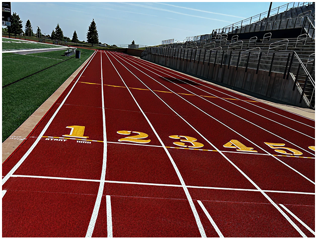 New running track construction with precision surface installation by Pro Track & Tennis Newly built red running track with yellow lane numbers and white starting lines beside stadium bleachers