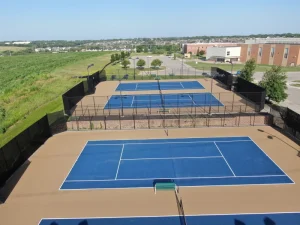 Aerial view of a resurfaced tennis court complex with bright blue playing surfaces and tan surrounding areas.