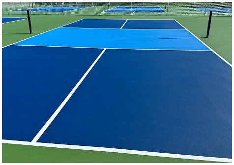 Newly constructed outdoor blue pickleball courts with white lines and durable acrylic surface beside green turf