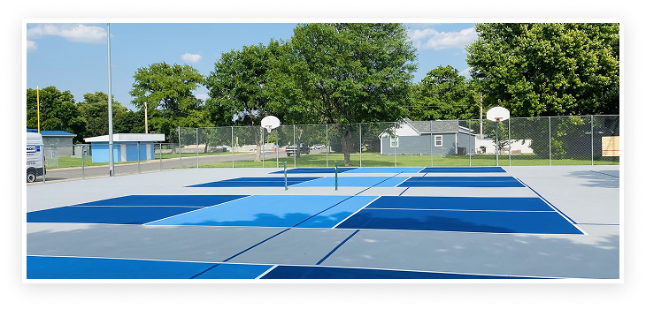 Blue and gray outdoor pickleball courts with precision-applied acrylic surface and basketball court nearby
