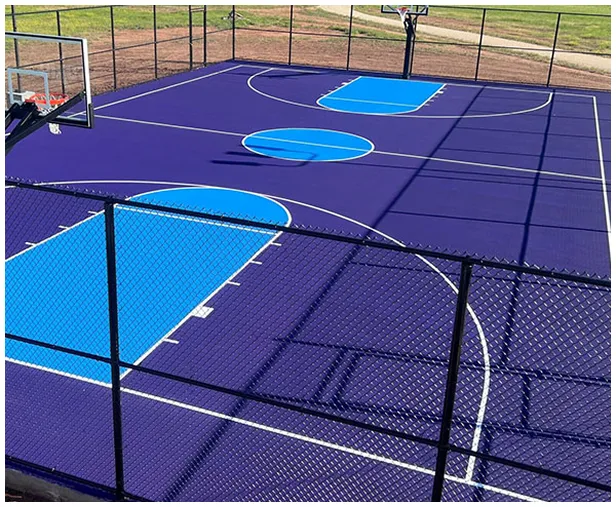Dark blue and light blue multi-purpose court with basketball hoops and clear line markings for multiple sports enclosed by fencing