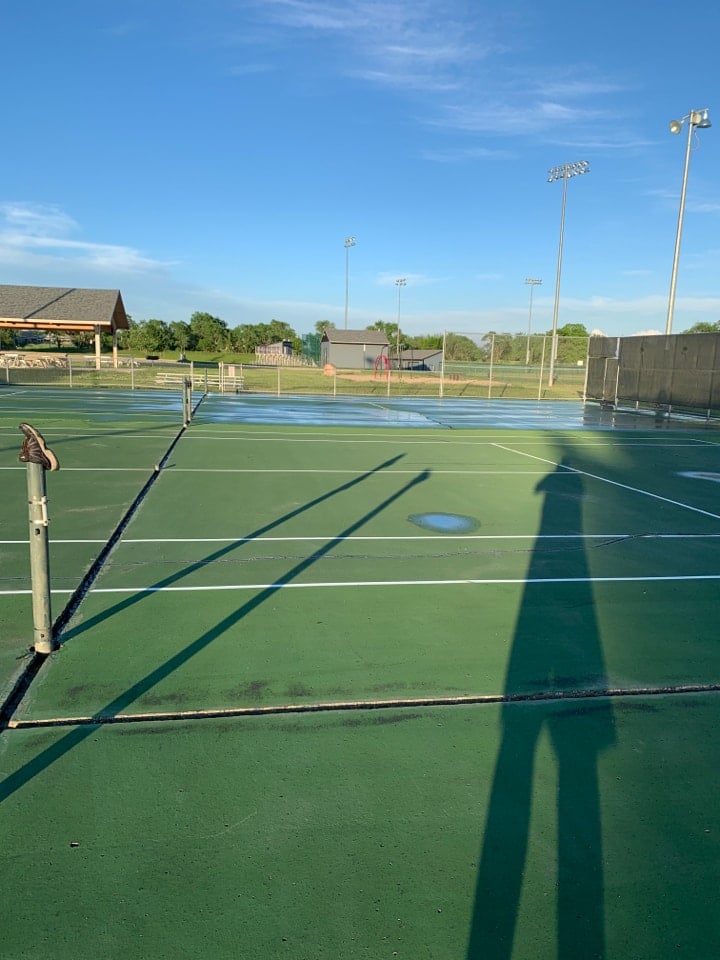 Tennis court showing early signs of birdbaths and drainage issues with minor puddles on the surface.