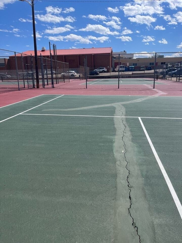 Tennis court with surface cracks and faded coating showing signs of UV damage before resurfacing.