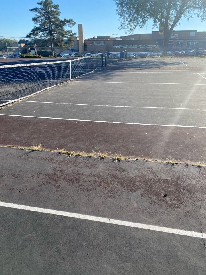 Worn tennis court surface showing wear and fading color before resurfacing by Pro Track & Tennis.