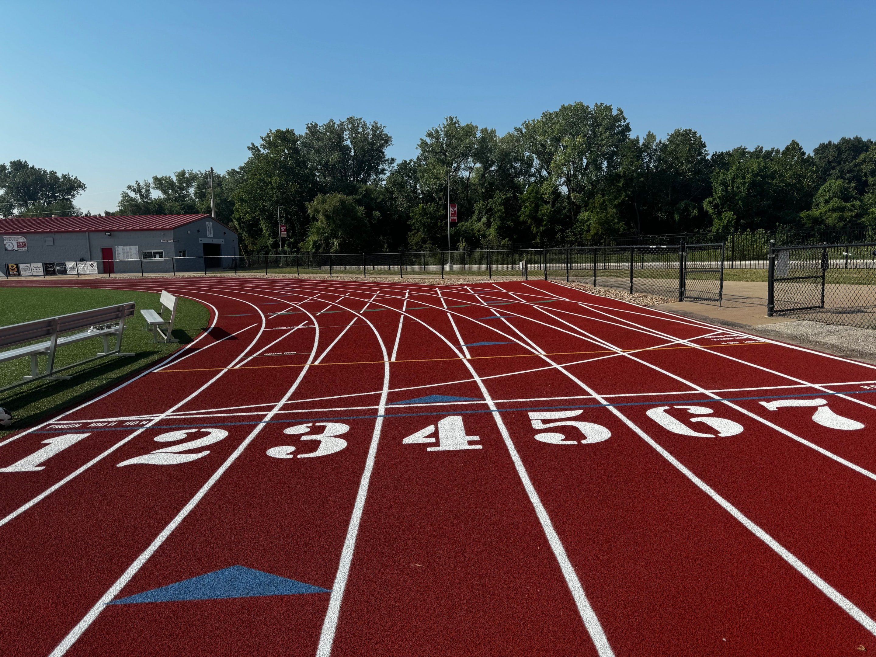 Rubber running track with fresh red surface and white lane numbers at a school facility.