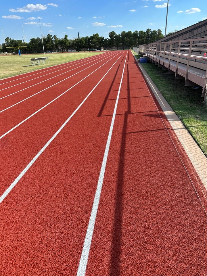 Freshly resurfaced rubber running track showing red textured surface and straight lane lines.