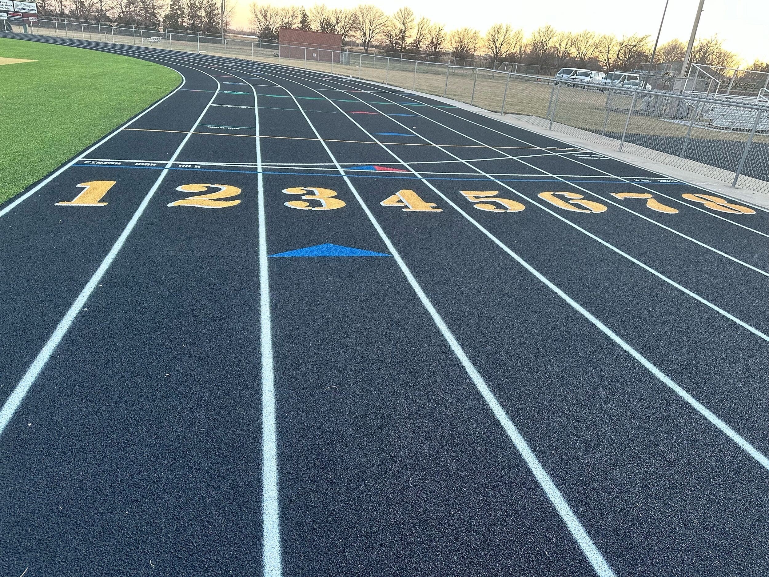 Completed running track installed by professional running track contractors with gold lane numbers and clear markings.