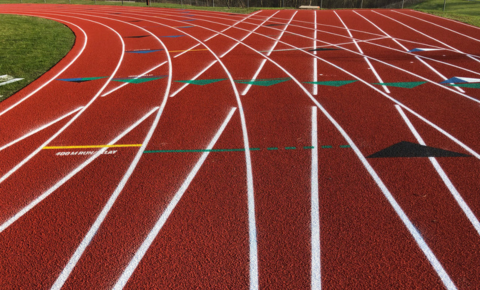 PTT WP Featured Image (11) Red all-weather running track with clear white lane lines and event markings under bright outdoor lighting.