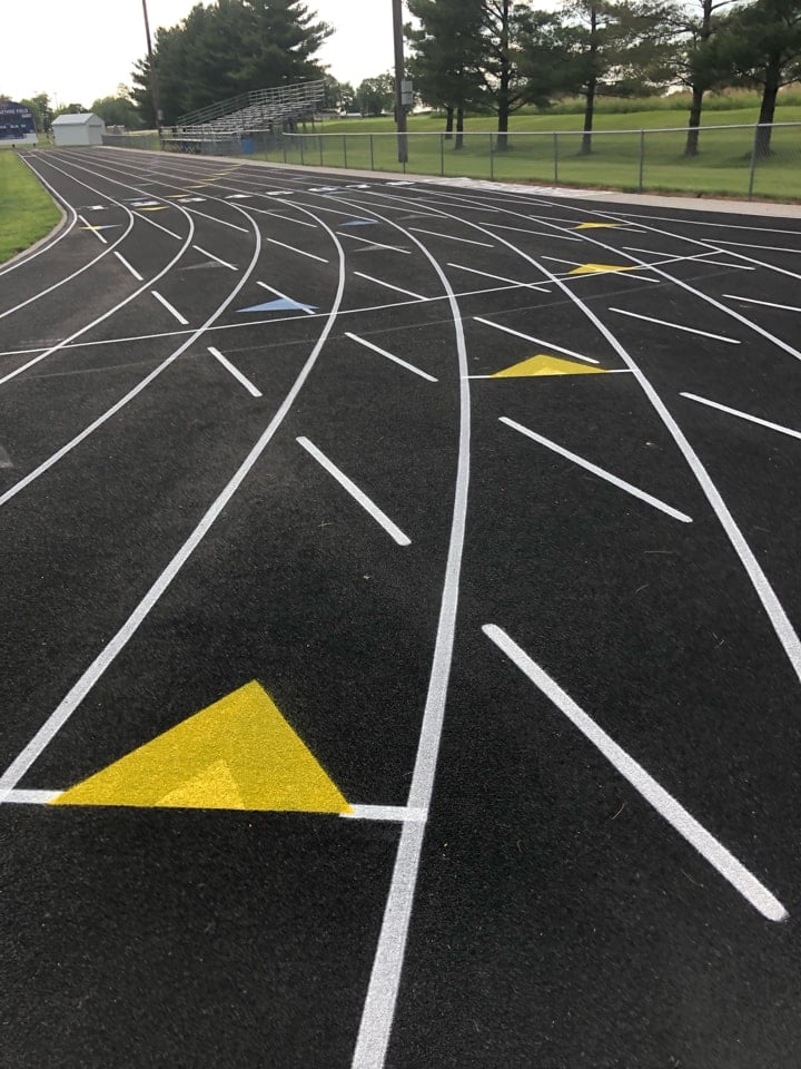 New running track surface with fresh white lane lines and yellow exchange arrows, showing resurfacing results in a track resurfacing vs rebuild comparison.