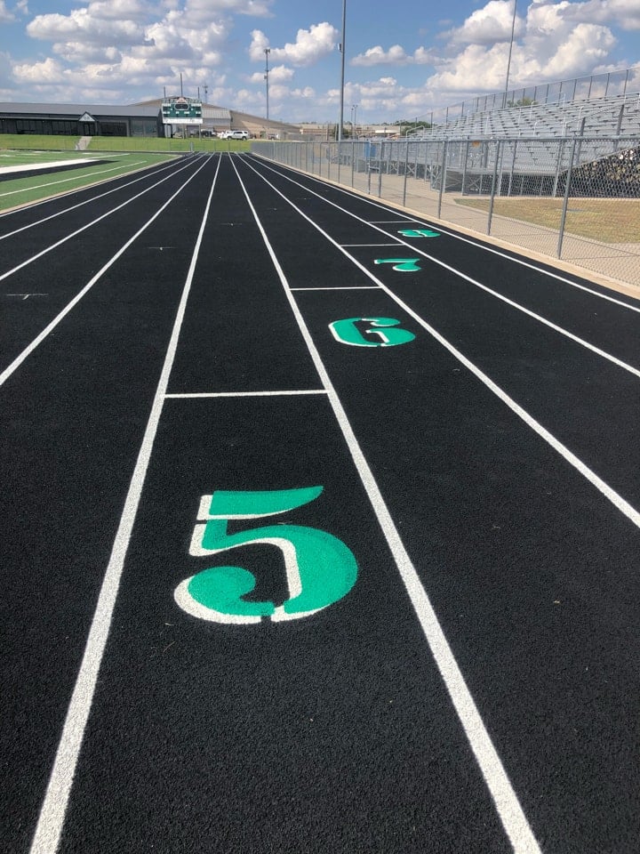 Finished outdoor running track with fresh black surface, bright white lane striping, and green lane numbers at a school athletic facility