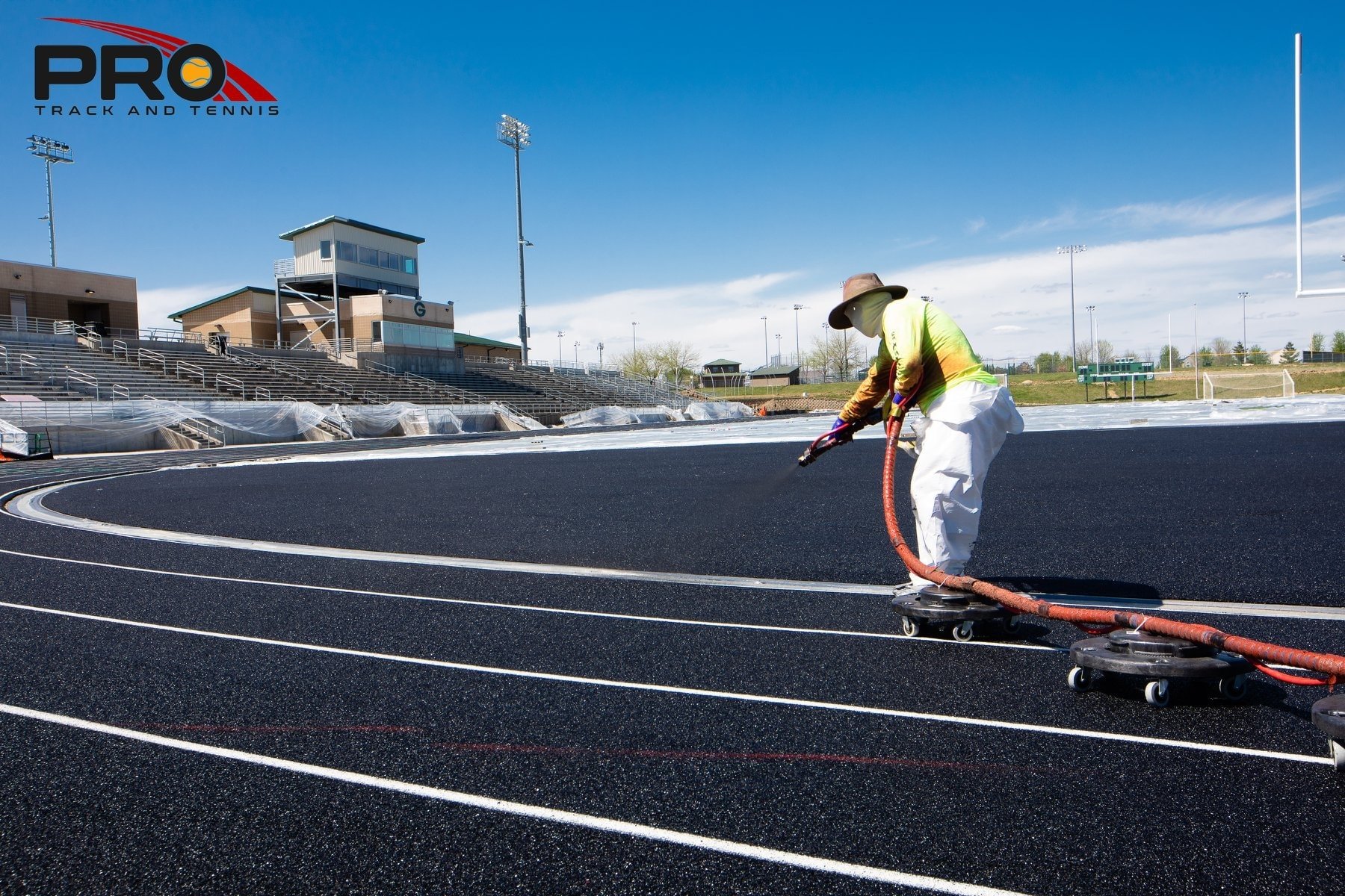 Running track construction in progress, showing a contractor applying a rubber track surface and lane markings at an outdoor athletic facility.
