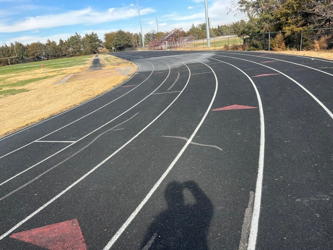 Running track construction assessment showing surface cracking, worn lane markings, and aging asphalt on an outdoor school track.