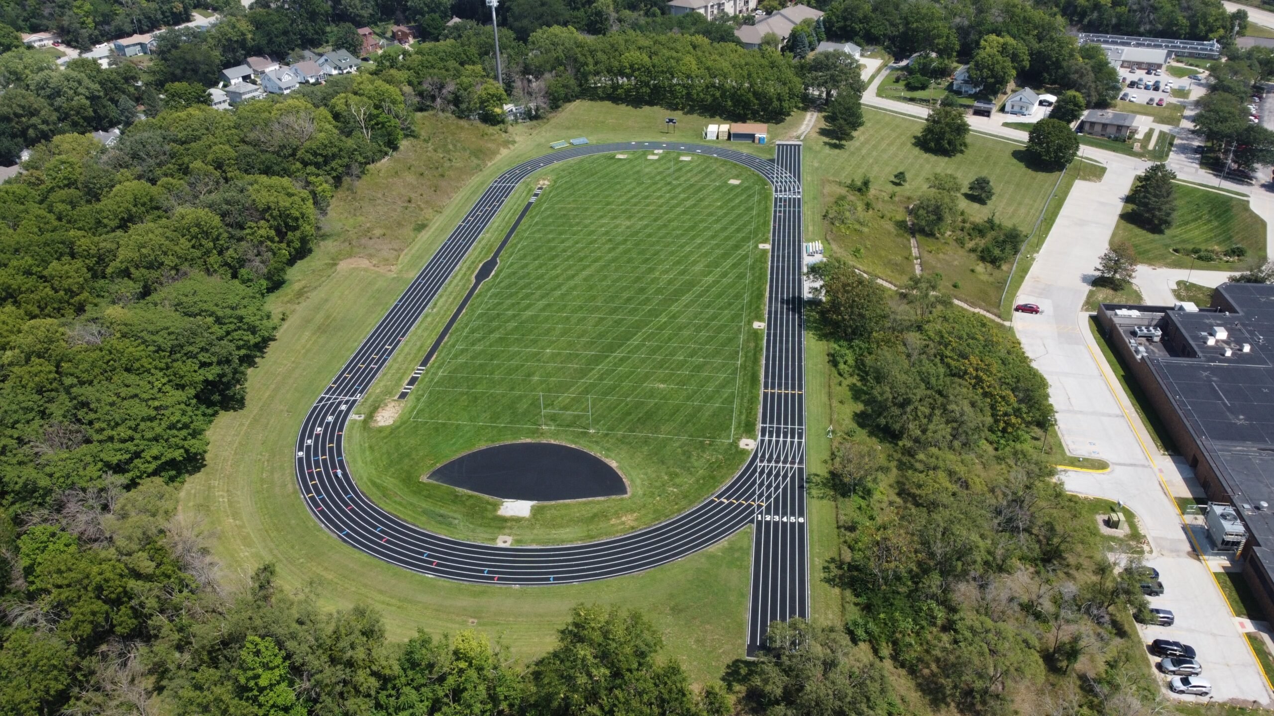 Aerial view of a high school running track and football field showing a standard 400-meter track layout and surrounding site conditions.
