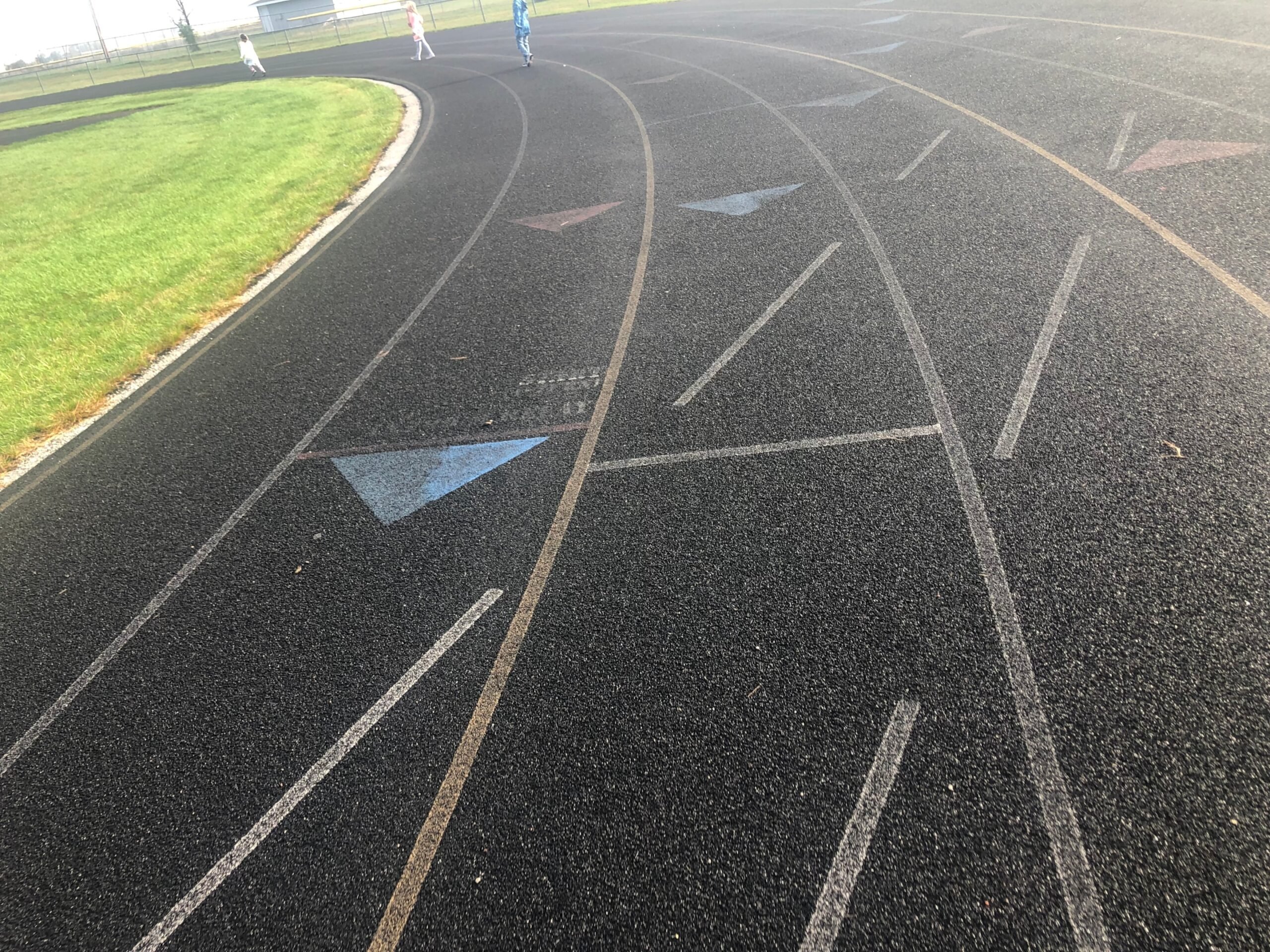 Curved section of a high school running track with worn and faded lane markings on a standard 400-meter surface.