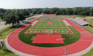 Aerial view of a red eight-lane running track surrounding a football field at a high school athletic stadium.