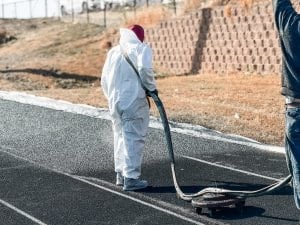 Crew member performing professional running track maintenance by applying a resurfacing or protective spray to the track surface.