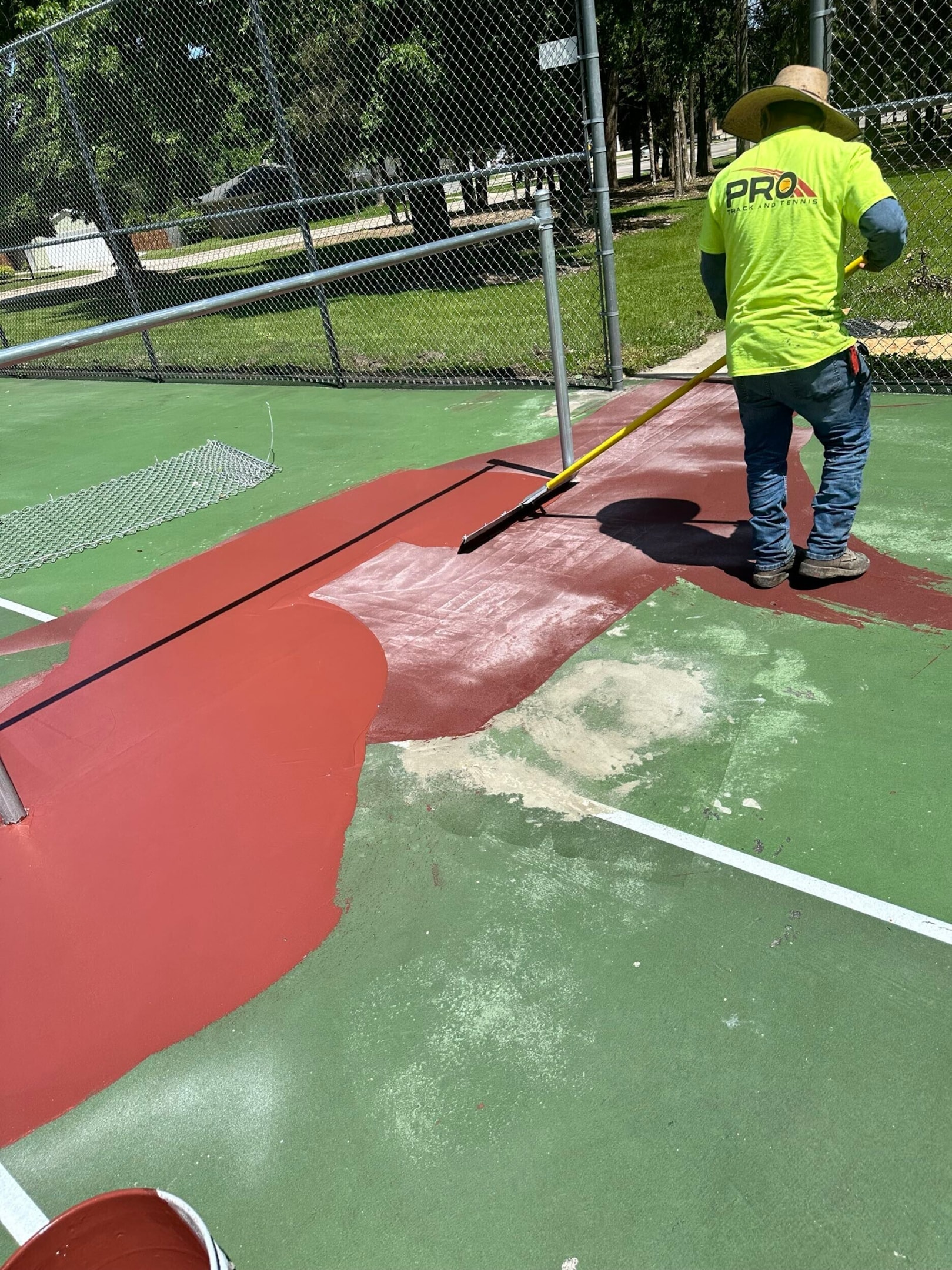 Tennis court resurfacing in progress with contractor applying acrylic coating to school court