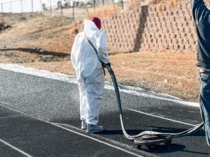 Crew installing synthetic track coating under proper temperature and dry conditions.