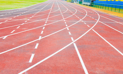 Worn out red rubber running track with faded lane markings and surface wear at school athletic facility