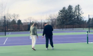 Athletic director inspecting school tennis court surface during budget planning evaluation