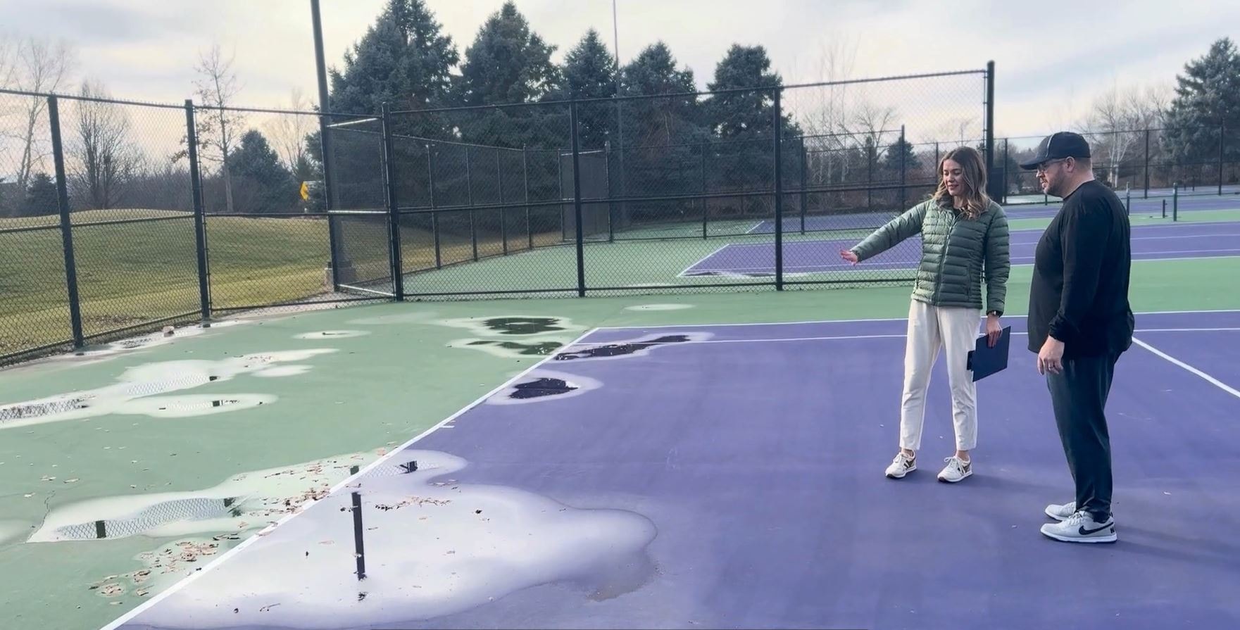 Athletic director inspecting puddling and surface damage on aging school tennis court for long-term budget planning