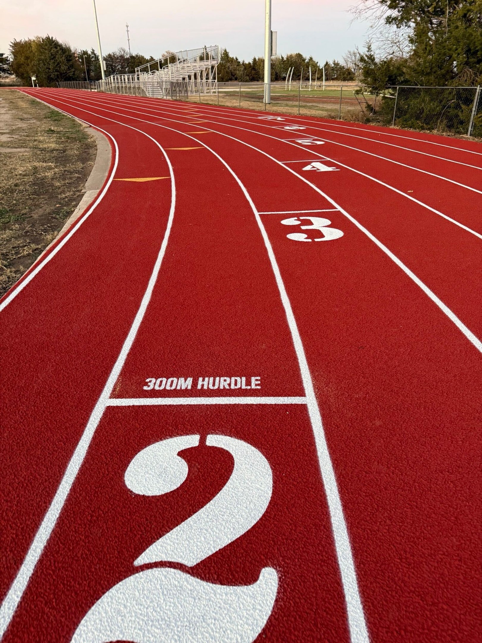 Red rubberized running track with lane numbers and 300 meter hurdle marking on the curve of a school athletics track