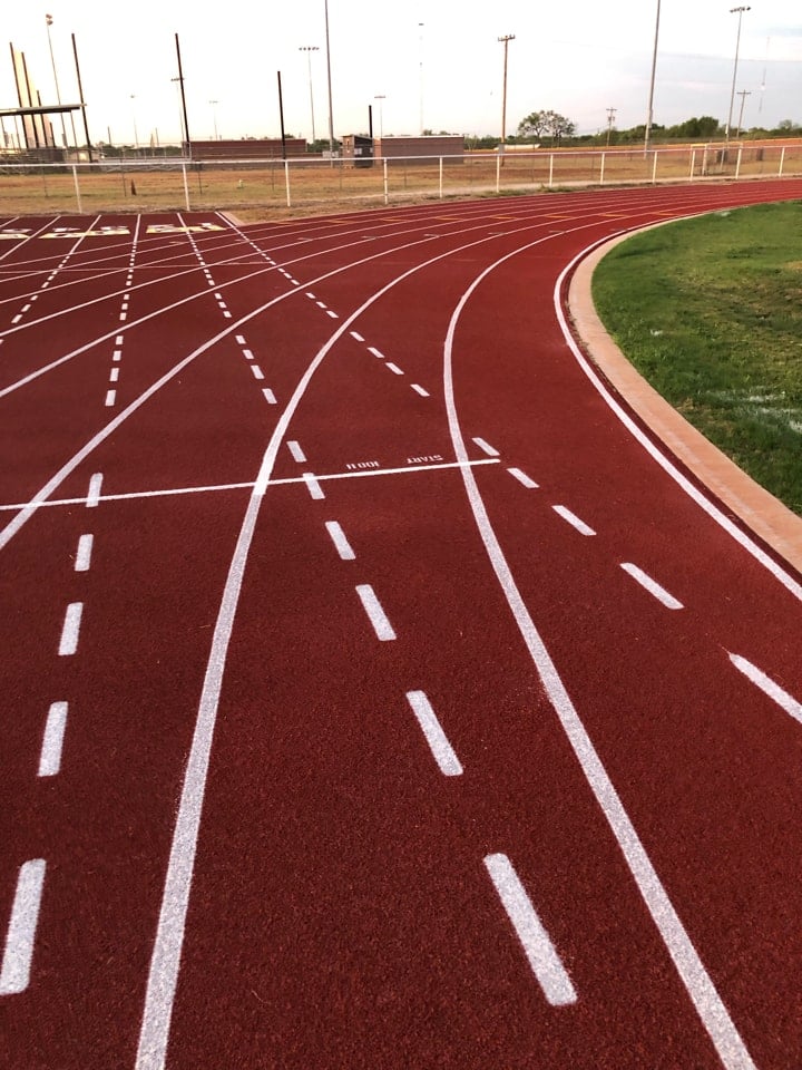Running track with clearly marked lanes and curves at an outdoor high school athletics facility showing standard track layout and lane markings