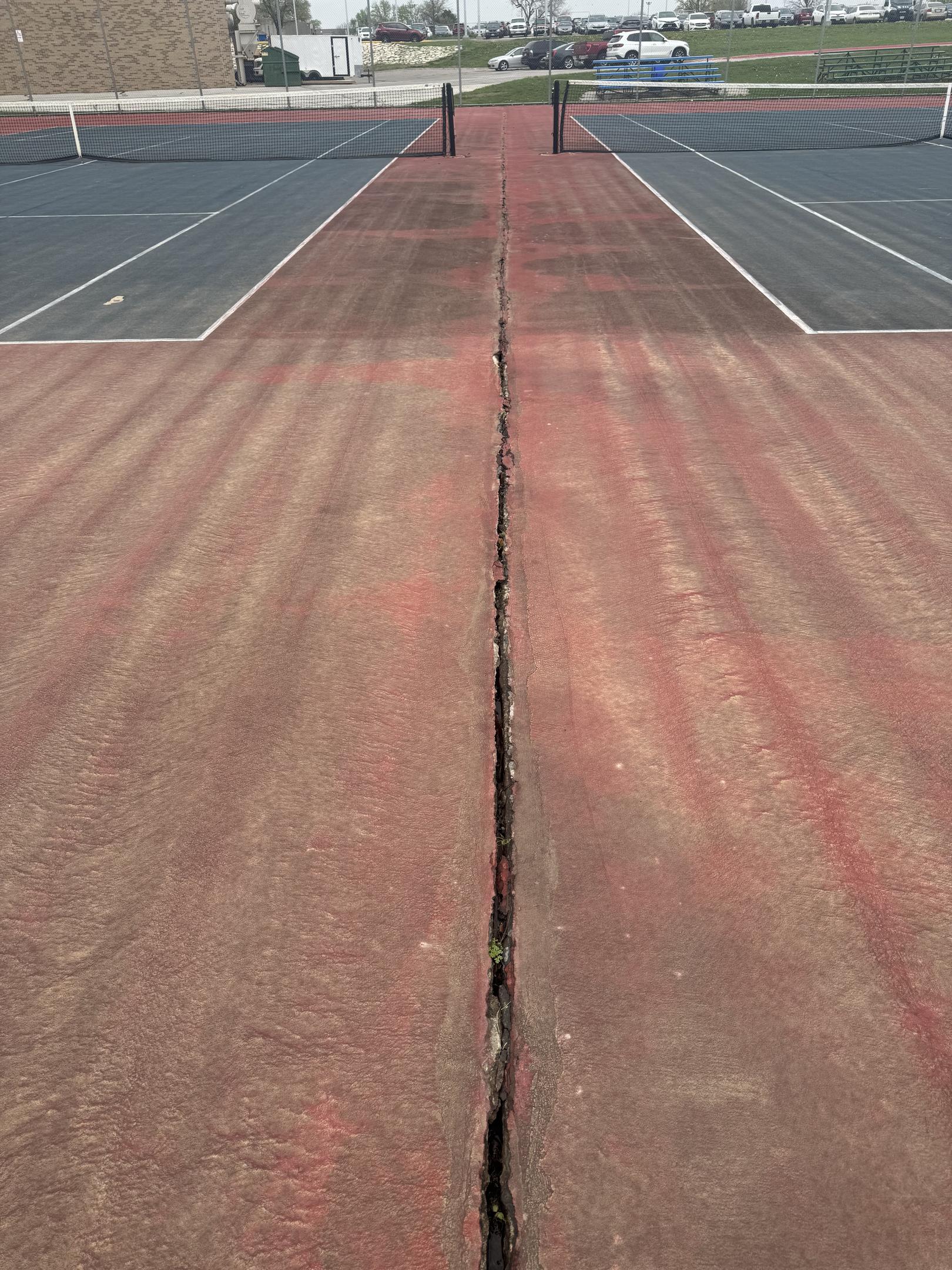Worn tennis court with surface cracks and fading showing need for resurfacing