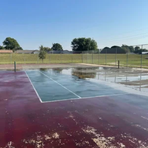Worn tennis court with standing water and peeling surface coating at Aaronson Park Tulsa before resurfacing