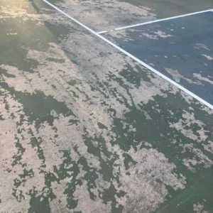 Close-up of deteriorated acrylic court surface with peeling layers on a pickleball and tennis court in Tulsa