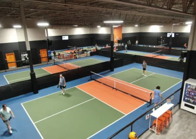 Overhead view of completed indoor pickleball facility with multiple courts in use, featuring green and orange court surfaces