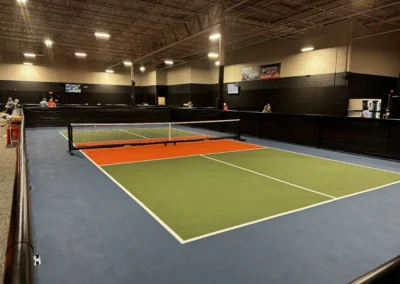 Completed indoor pickleball court showing green and orange color coat surface with black perimeter fencing