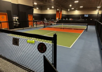 Indoor pickleball courts viewed through perimeter fencing with player seating and facility amenities in background