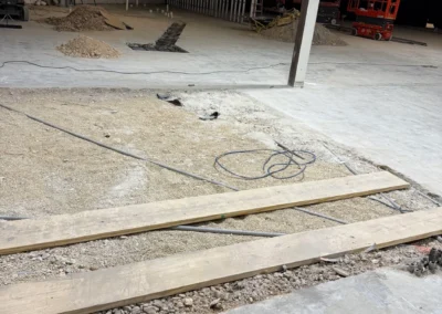 Indoor court construction site showing concrete subfloor preparation with gravel base and lumber forms at Red Oak High School