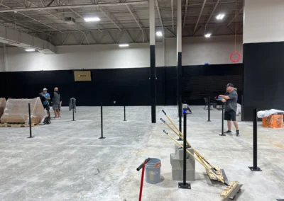 Pro Track and Tennis crew installing net posts on concrete surface during indoor tennis court construction