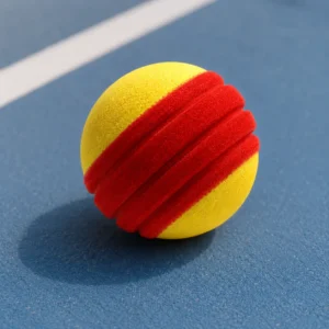 Close-up of a yellow and red channeled TYPTI foam ball resting on a blue court surface.