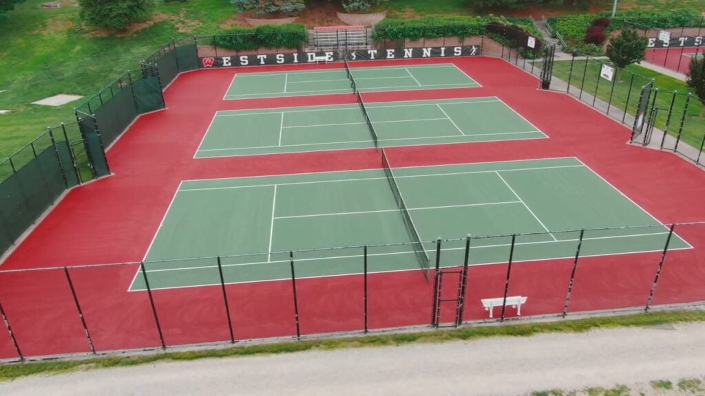 Aerial view of resurfaced Westside High School tennis courts with grass green playing areas, red out-of-bounds zones, and fresh white striping.