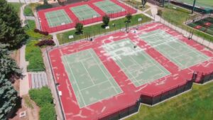 Aerial view of Westside High School tennis courts during surface preparation, showing patched areas across the red and green court surface.
