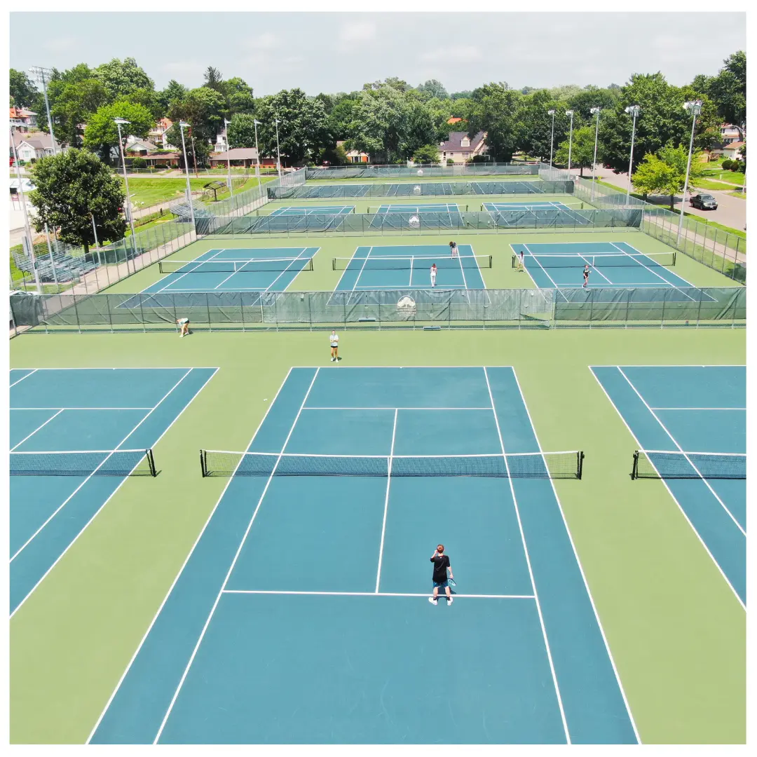 Aerial view of multiple outdoor tennis courts with players in sunny conditions.
