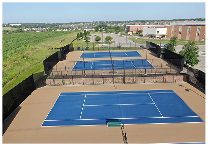 Aerial view of newly resurfaced blue tennis courts with tan surrounds at a school or community facility.