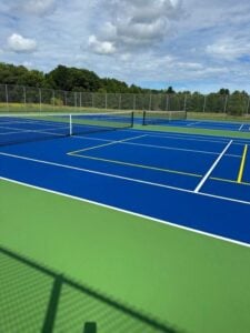Blue and green pickleball courts at Suamico Village with fencing and open grass fields in the background.